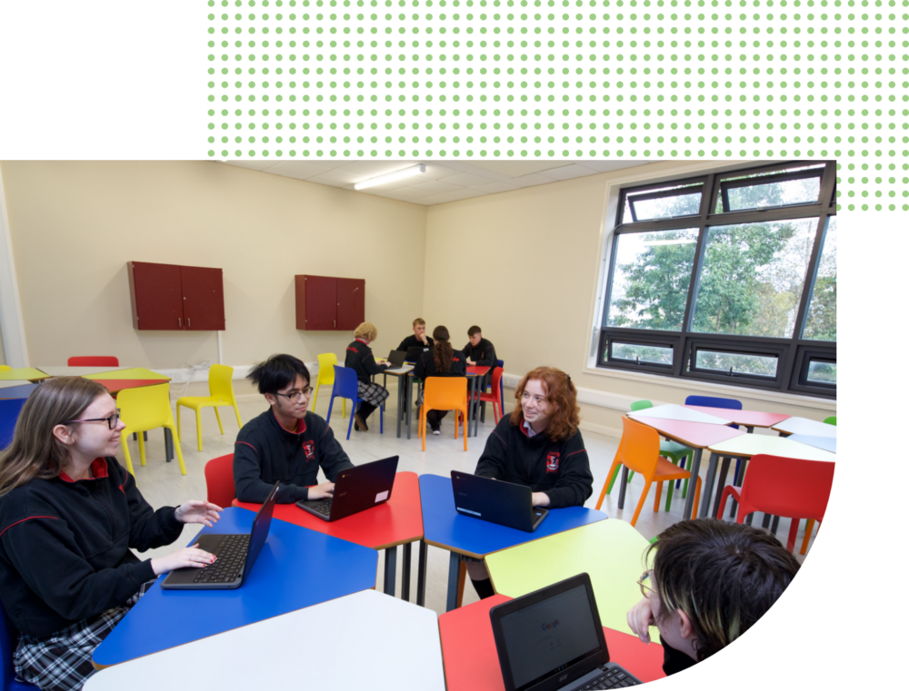 students sitting at desks in a circle in a classroom with laptops
