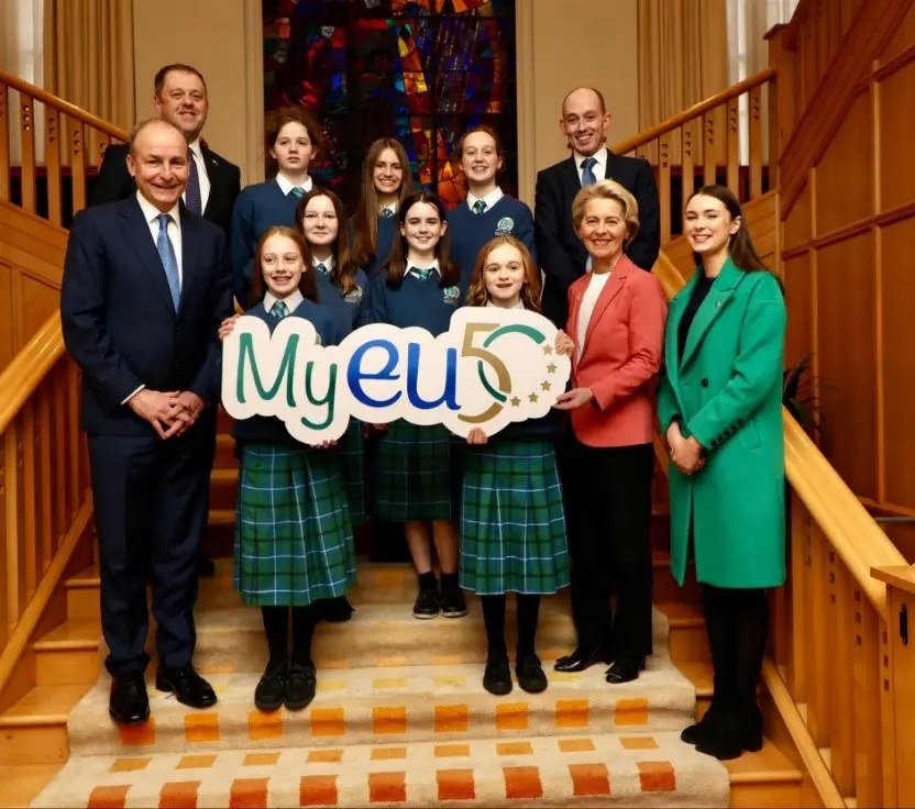 Group of Gaelcholáiste Mhaigh Nuad students standing with the class tutor, the President of the European Commission, the Taoiseach, and the Minister of State for European Affairs holding a 'My EU 50' sign 