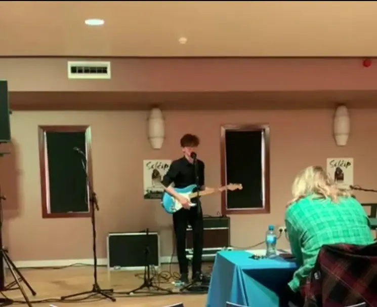 Gaelcholáiste Mhaigh Nuad student performing his electrical guitar in front of judges 