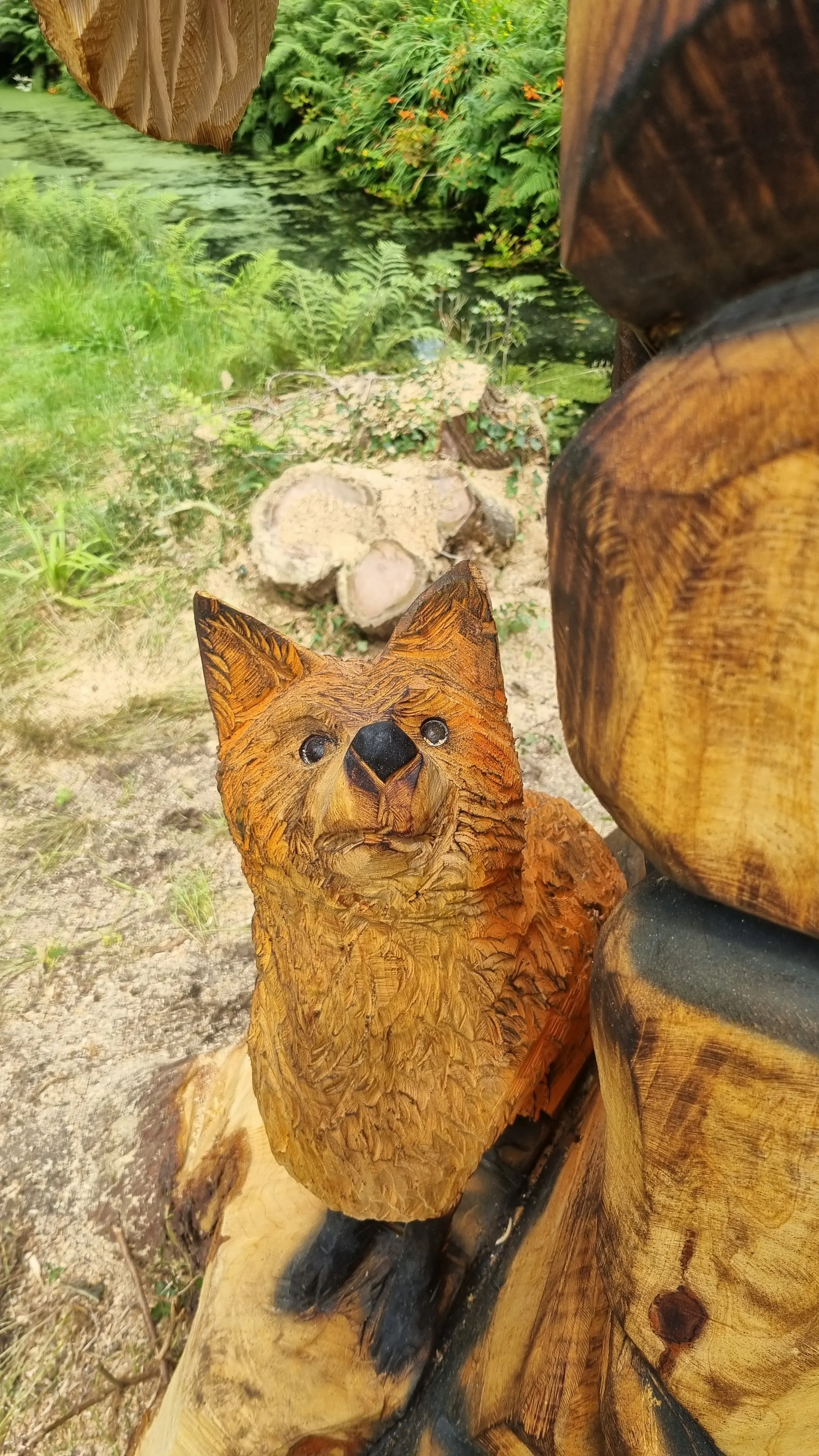 Wooden fox carving beside a pond with greenery in the background