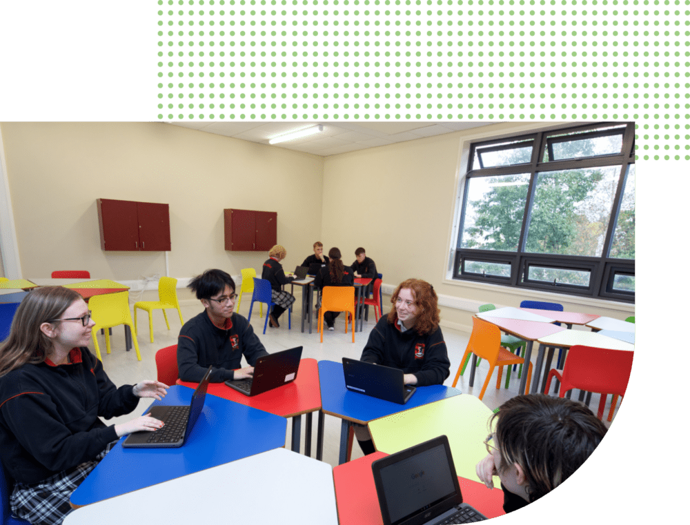 students sitting at desks in a circle in a classroom with laptops