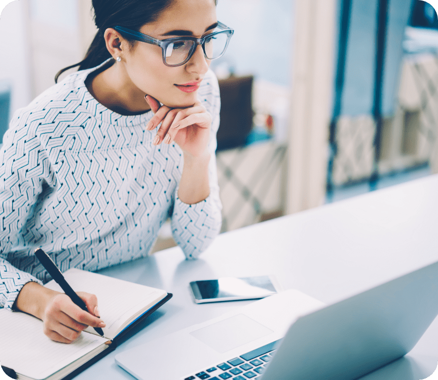 girl looking at laptop screen and writing notes
