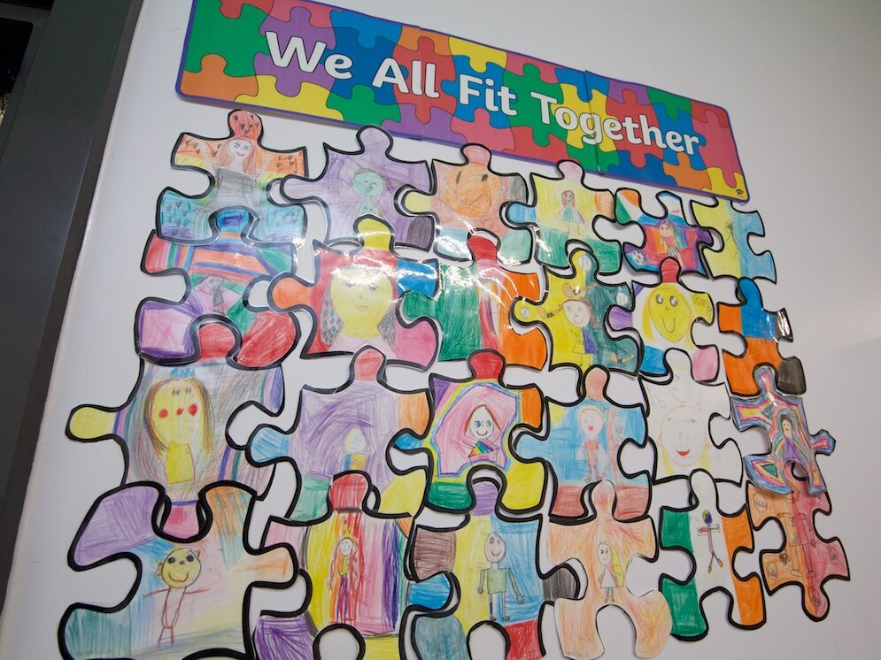 Caption "We all Fit together" jigsaw pieces hand coloured and joined together on display